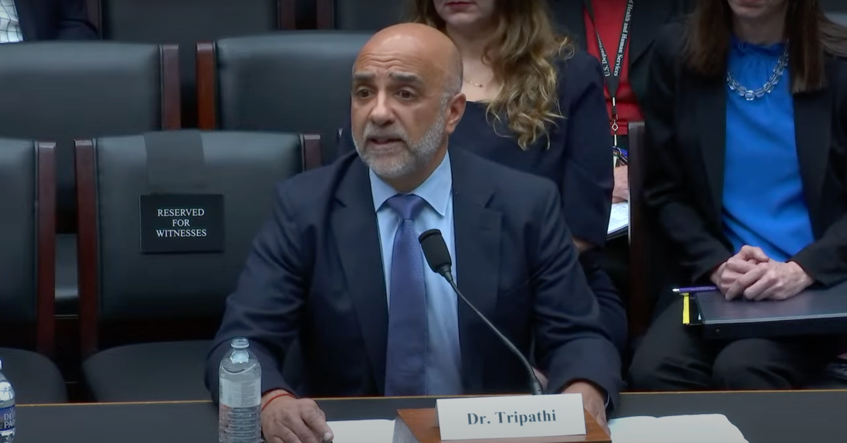 Micky Tripathi pictured sitting at a desk as a witness for a hearing on Capitol Hill. He wears a suit and has a name placard in front of him that reads "Dr. Tripathi."